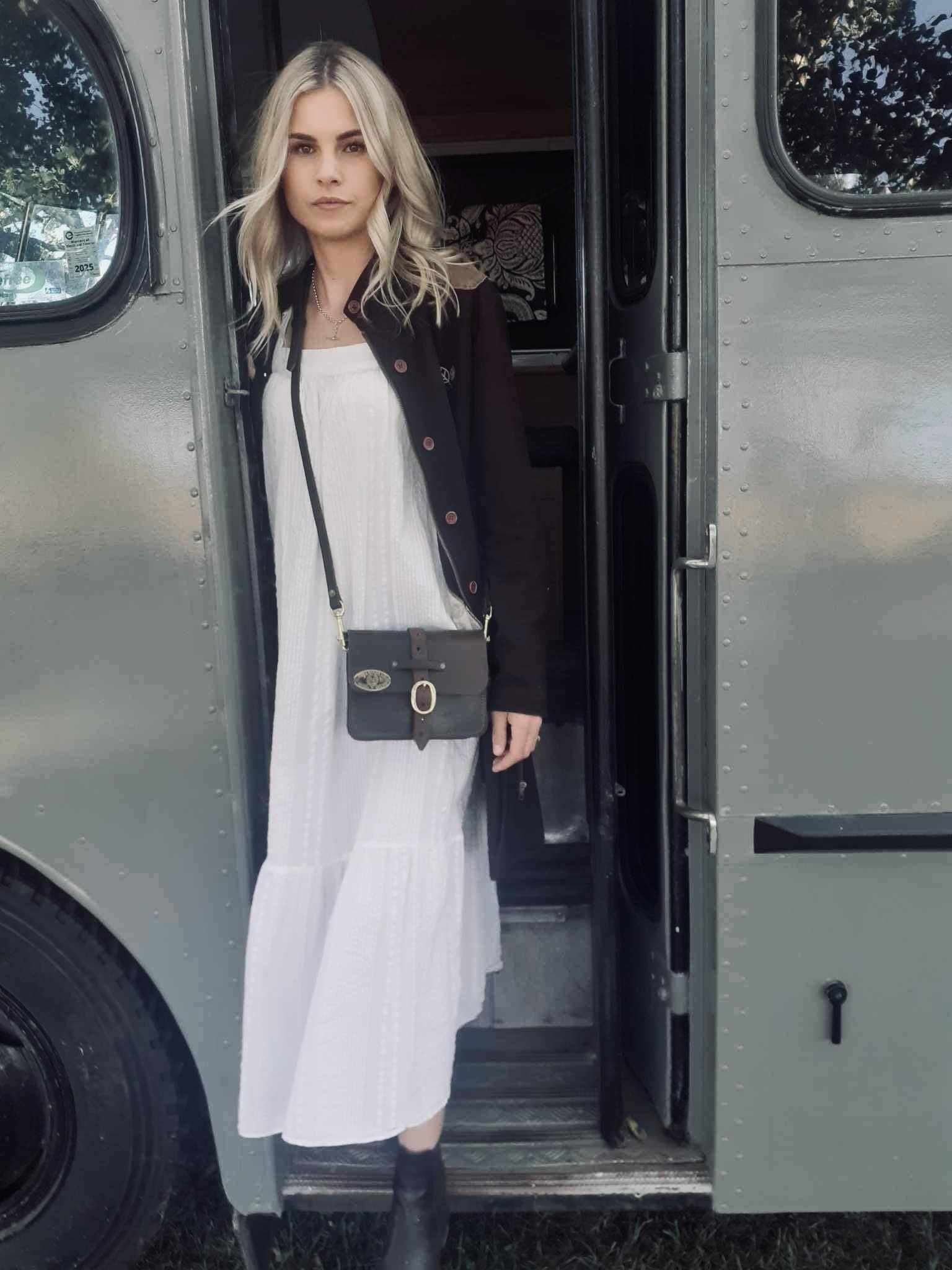Girl-stepping-down-from-vintage-bus-with-white-dress-and-vintage-leather-bag