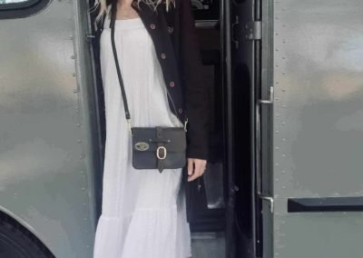Girl stepping down from vintage bus with white dress and vintage leather bag